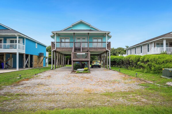 A two-story house with a covered porch and a gravel driveway. - Capt Roy's: Captain Roy's: Charming Dog-Friendly Third Row Cottage (Oak Island)