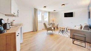 A modern kitchen with a coffee machine, a dining area with a table and chairs, a sofa, and a flat-screen TV mounted on the wall. - Résidence du Parc Vanves (Vanves)