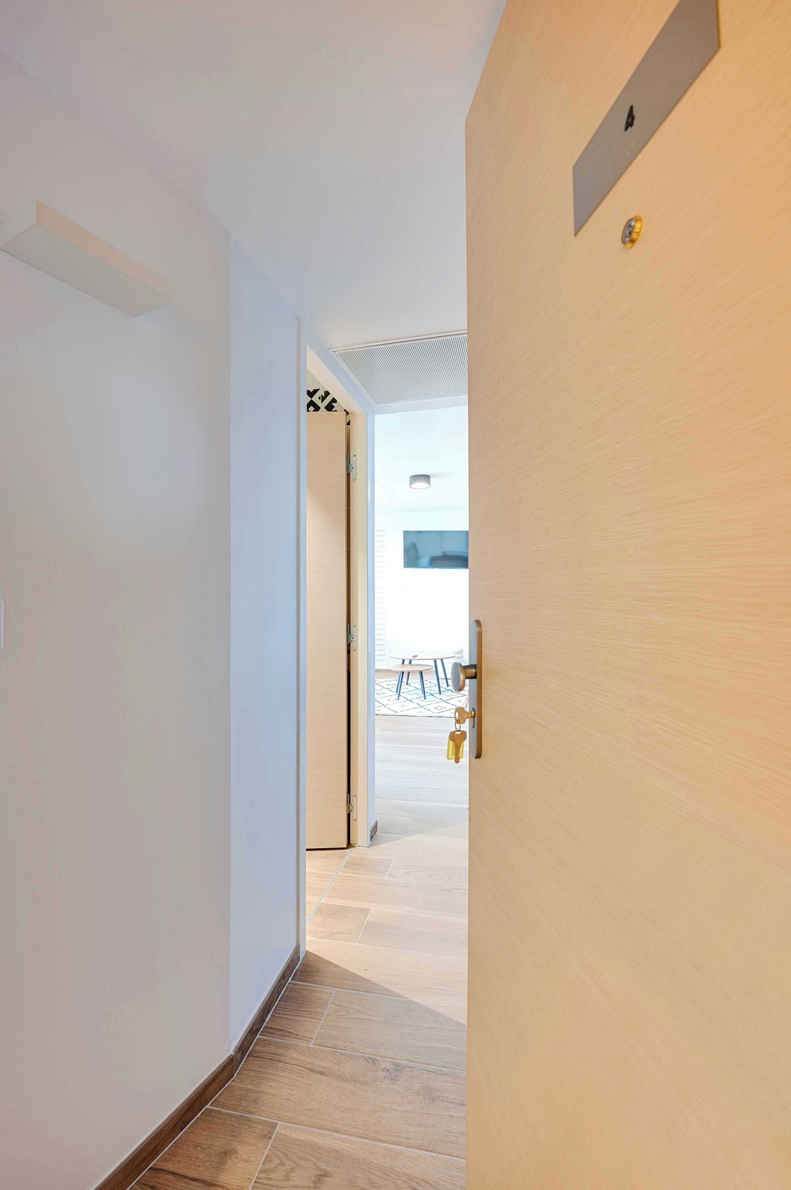A hallway with a wooden door, a light switch, and a wall-mounted light fixture.