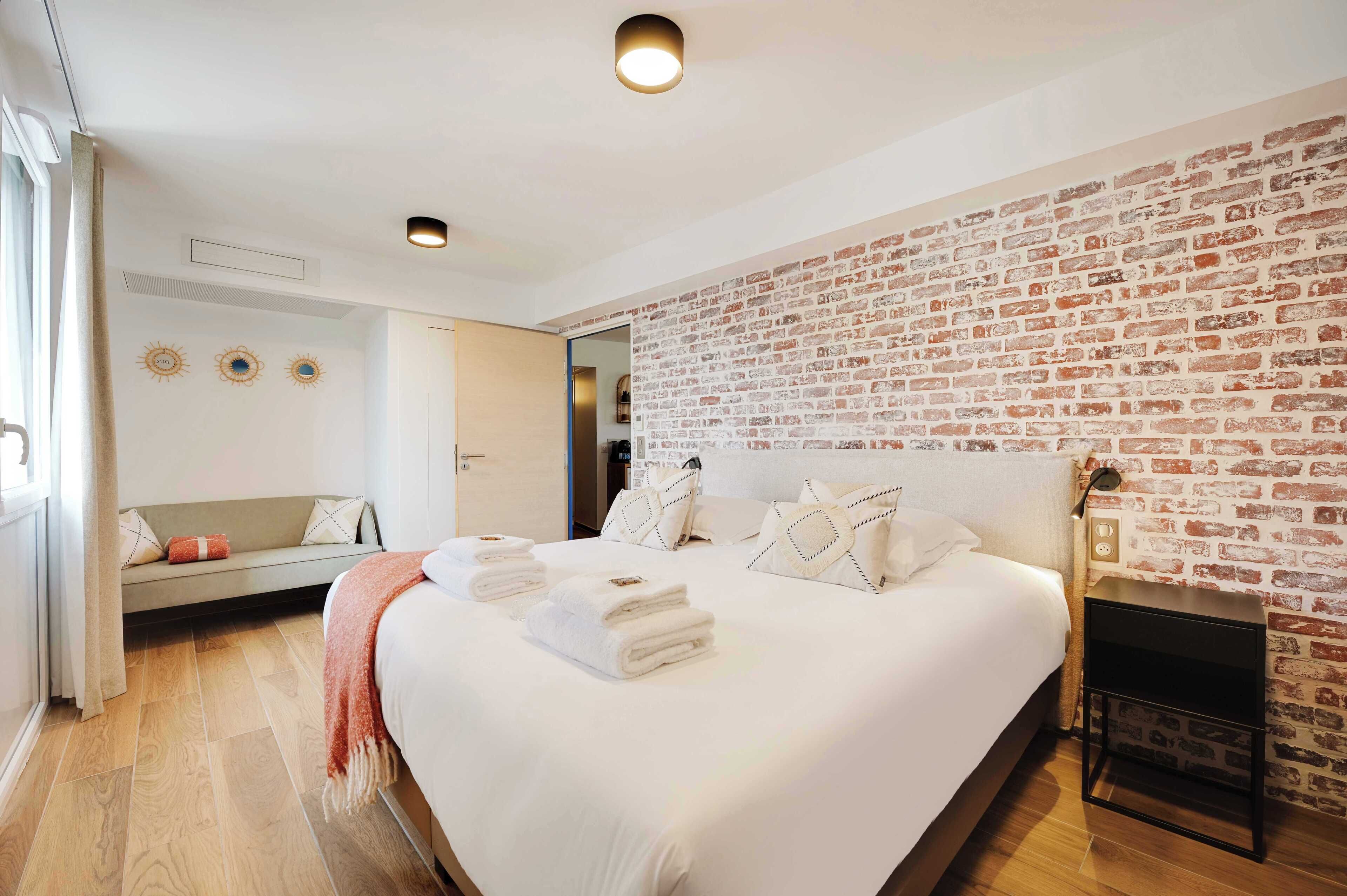 Un dormitorio moderno con una cama grande, una pared con diseño de ladrillo, un pequeño rincón de descanso y una chimenea.