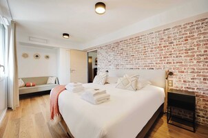 Un dormitorio moderno con una cama grande, una pared con diseño de ladrillo, un pequeño rincón de descanso y una chimenea.