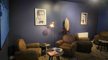A lounge area with brown leather armchairs, a small table with magazines, a floor lamp, and two framed pictures on the wall.