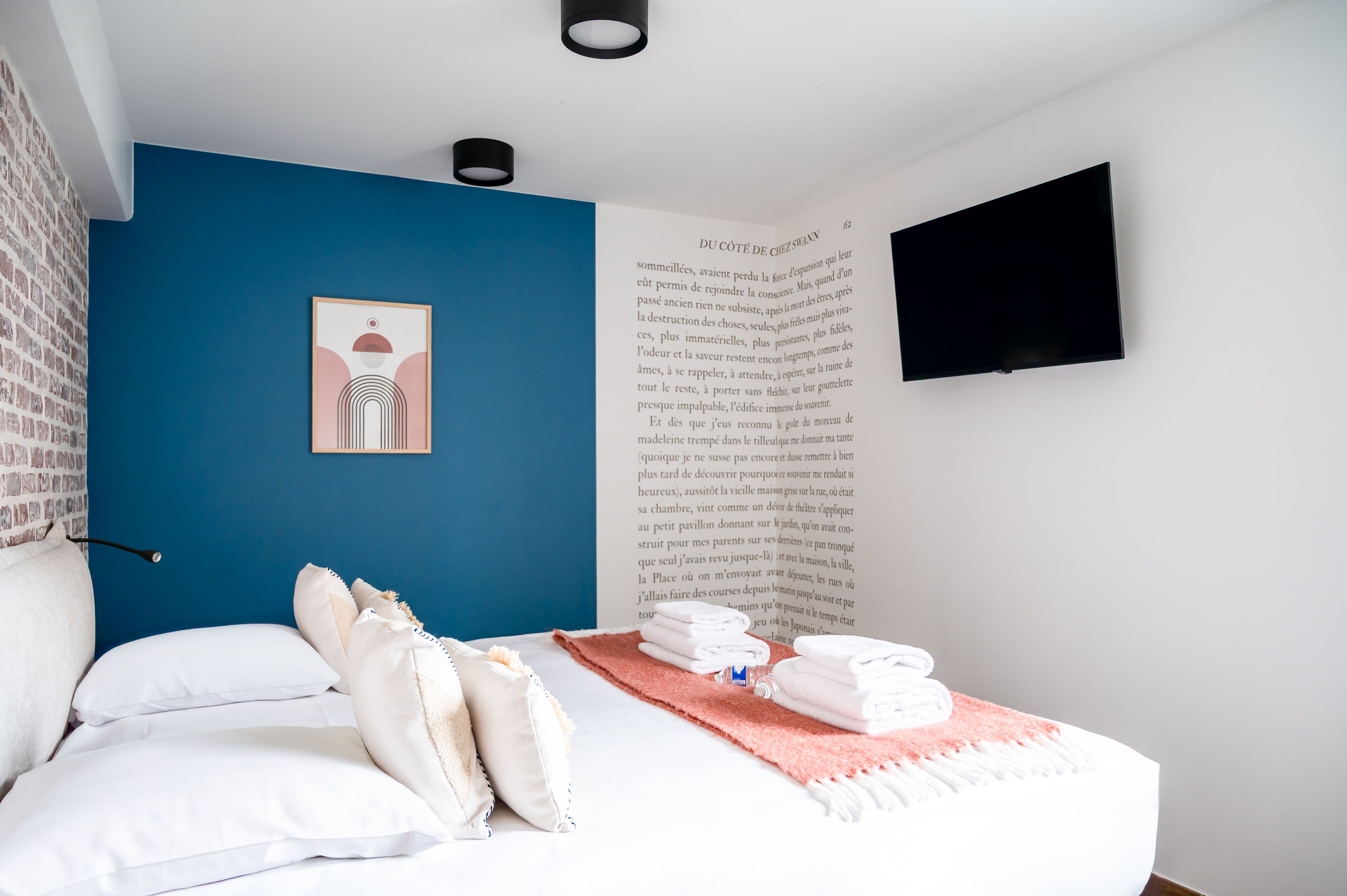 A bedroom with a blue accent wall, a bed with white bedding, a pink throw, and a book on the wall.