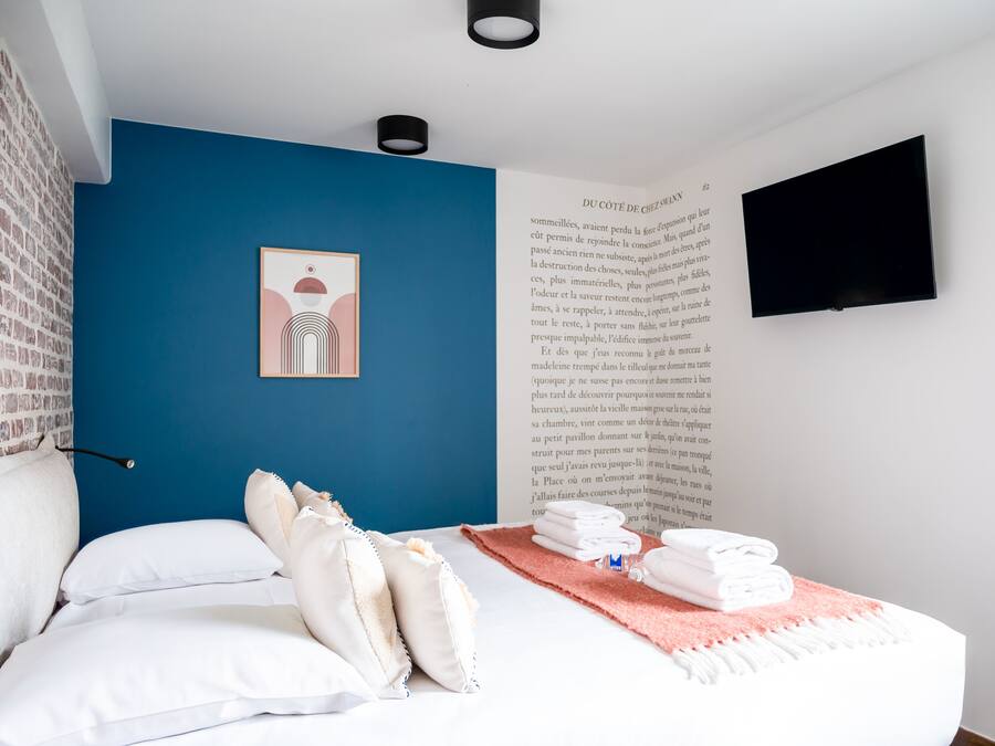 A bedroom with a blue accent wall, a bed with white bedding, a pink throw, and a book on the wall.
