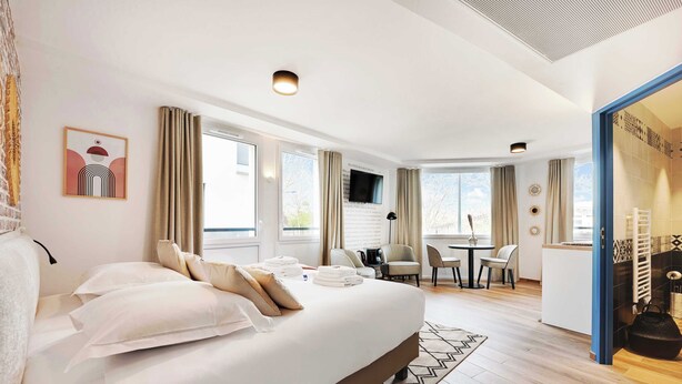 A hotel room with a large bed, a desk, and a chair. There is a television on the wall and a window with curtains. - Résidence du Parc Vanves (Vanves)