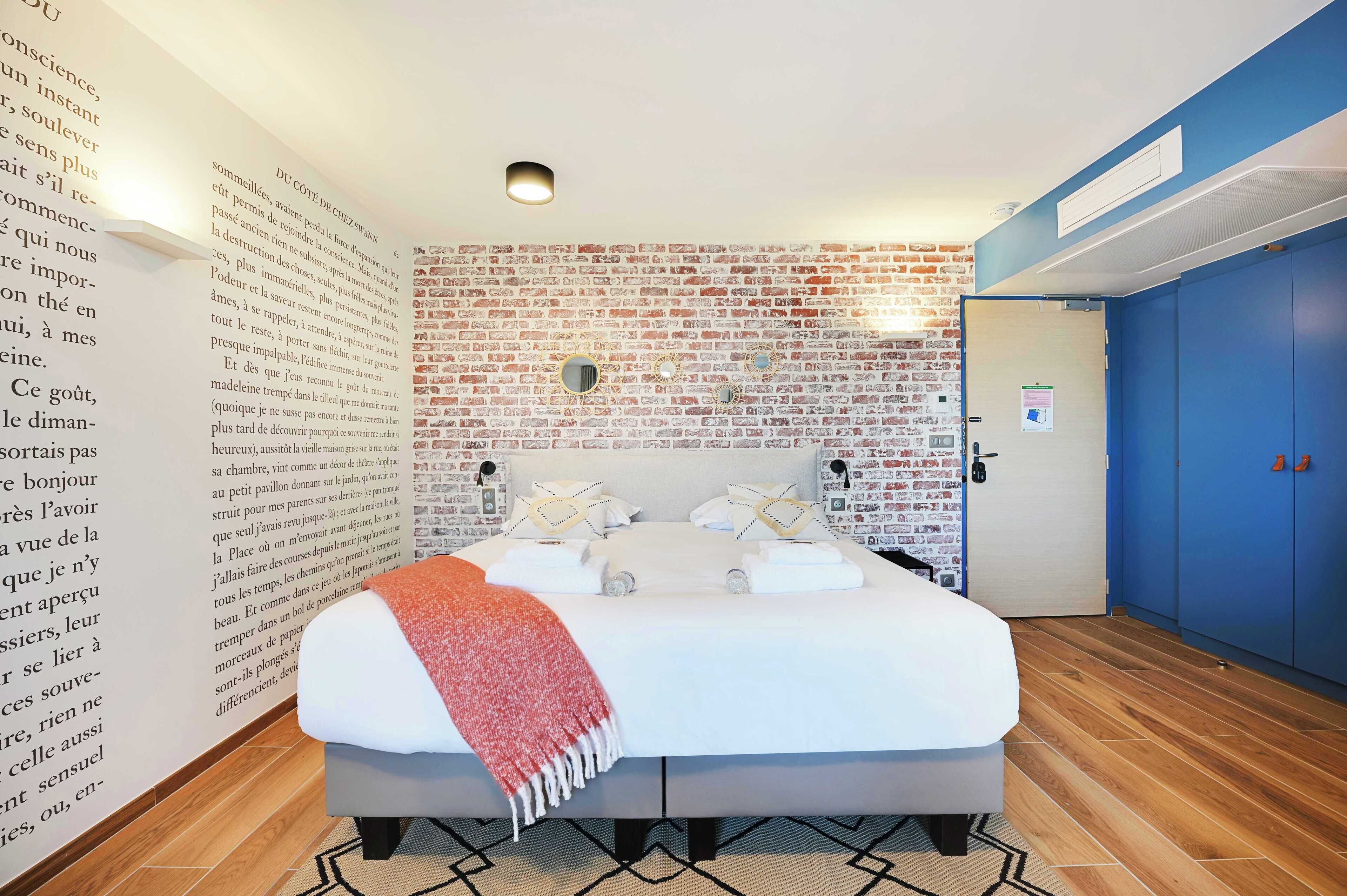 A bedroom with a brick-patterned wall, a bed with white linens, and a blue wardrobe.