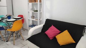 A compact living space with a black sofa, colorful chairs, a white bookshelf, and a small dining table. - Magnifico Apartamento Central (Curitiba)