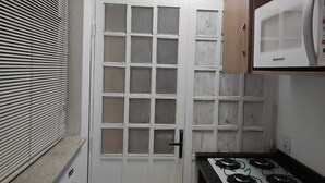 A compact kitchen with a gas stove, a microwave, and a white door with a grid pattern. - Magnifico Apartamento Central (Curitiba)