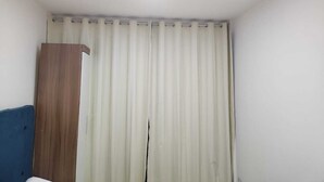 A room with a single bed, a wooden wardrobe, and a window with white curtains. - Magnifico Apartamento Central (Curitiba)