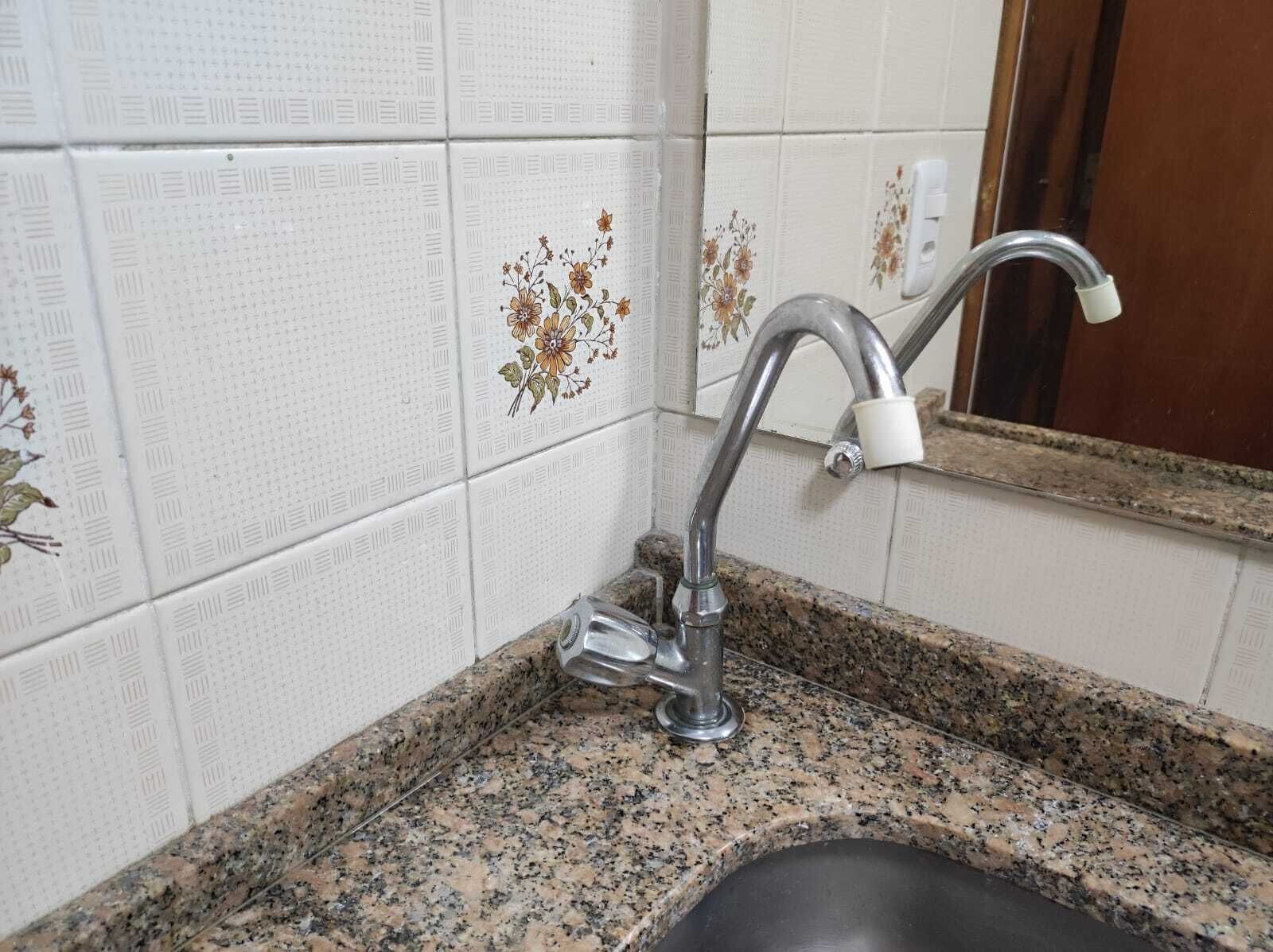 A bathroom with white tiled walls, a granite countertop, and a sink with a faucet.