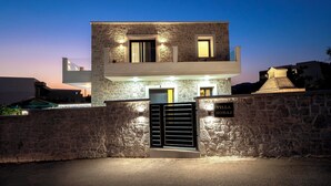 A modern two-story stone building with a gated entrance, a sign reading "Villa Hodaj," and a balcony with lights.