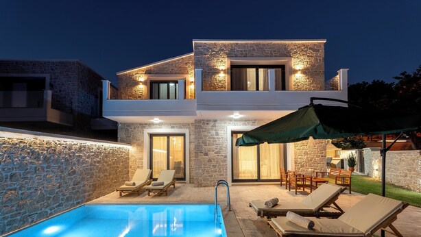 A modern two-story house with a swimming pool, outdoor seating, and stone walls.