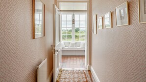 Un couloir avec un papier peint à motifs, un radiateur, un tapis à motifs et un banc de fenêtre d’où l’on peut admirer le paysage extérieur.