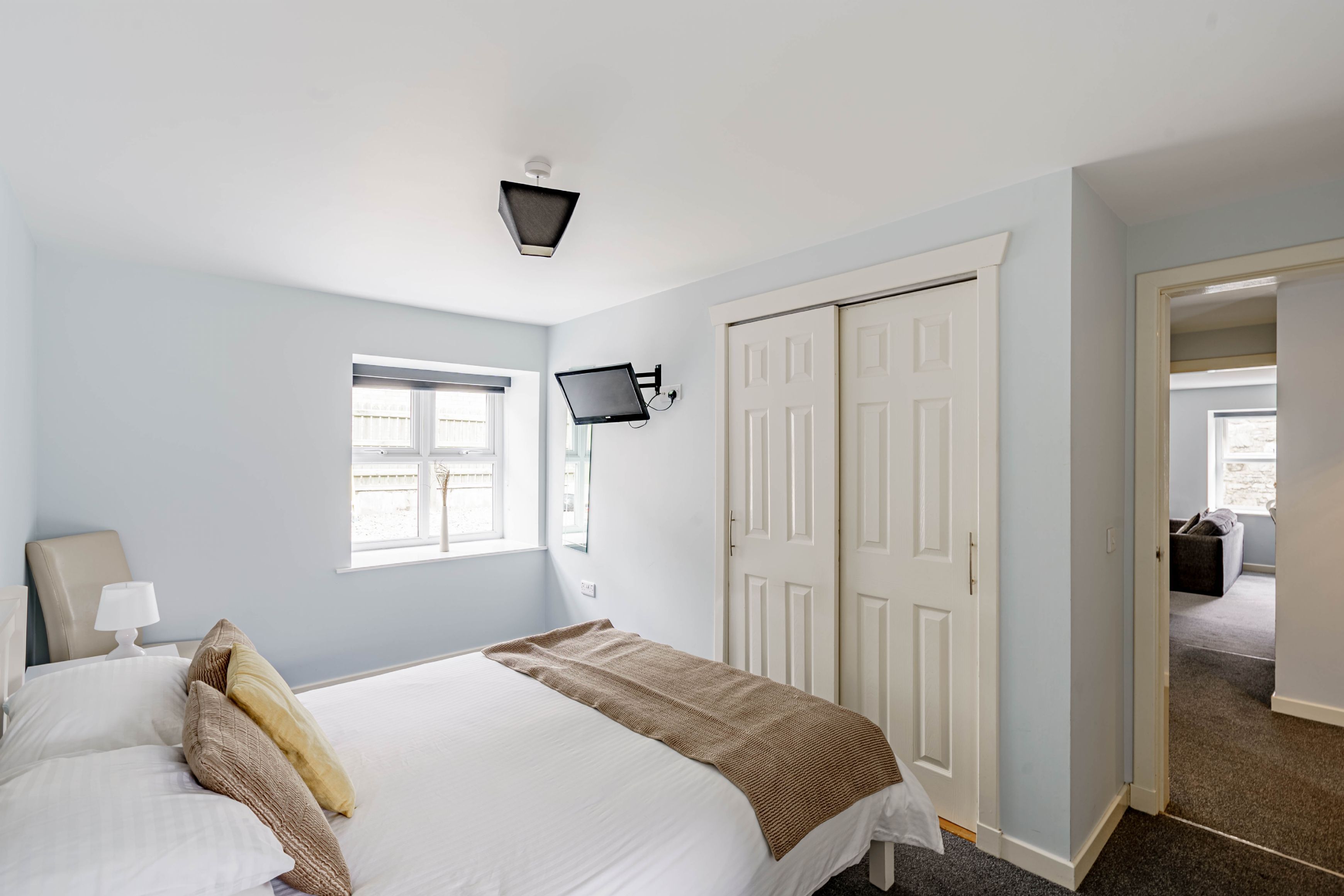 A bedroom with a bed, a bedside table, a lamp, a TV, and a wardrobe.