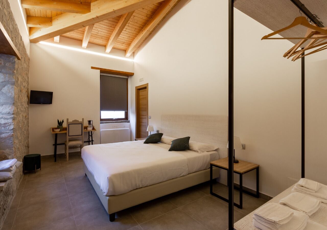 A bedroom with a bed, a desk, a chair, a TV, and a wooden ceiling.