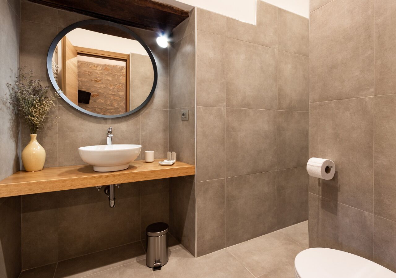 A modern bathroom with a round mirror, a beige sink, and a toilet.