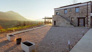 A modern stone building with a staircase leading to the entrance, surrounded by a gravel courtyard with potted plants. - Tenuta San Martino (Nusco)