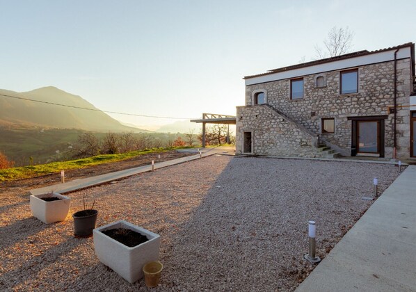 A modern stone building with a staircase leading to the entrance, surrounded by a gravel courtyard with potted plants. - Tenuta San Martino (Nusco)