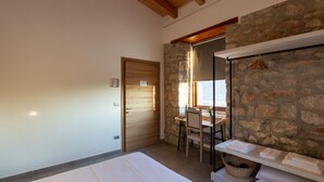 A bedroom with a wooden door, a stone wall, a desk with a chair, and a shelf with towels. - Tenuta San Martino (Nusco)