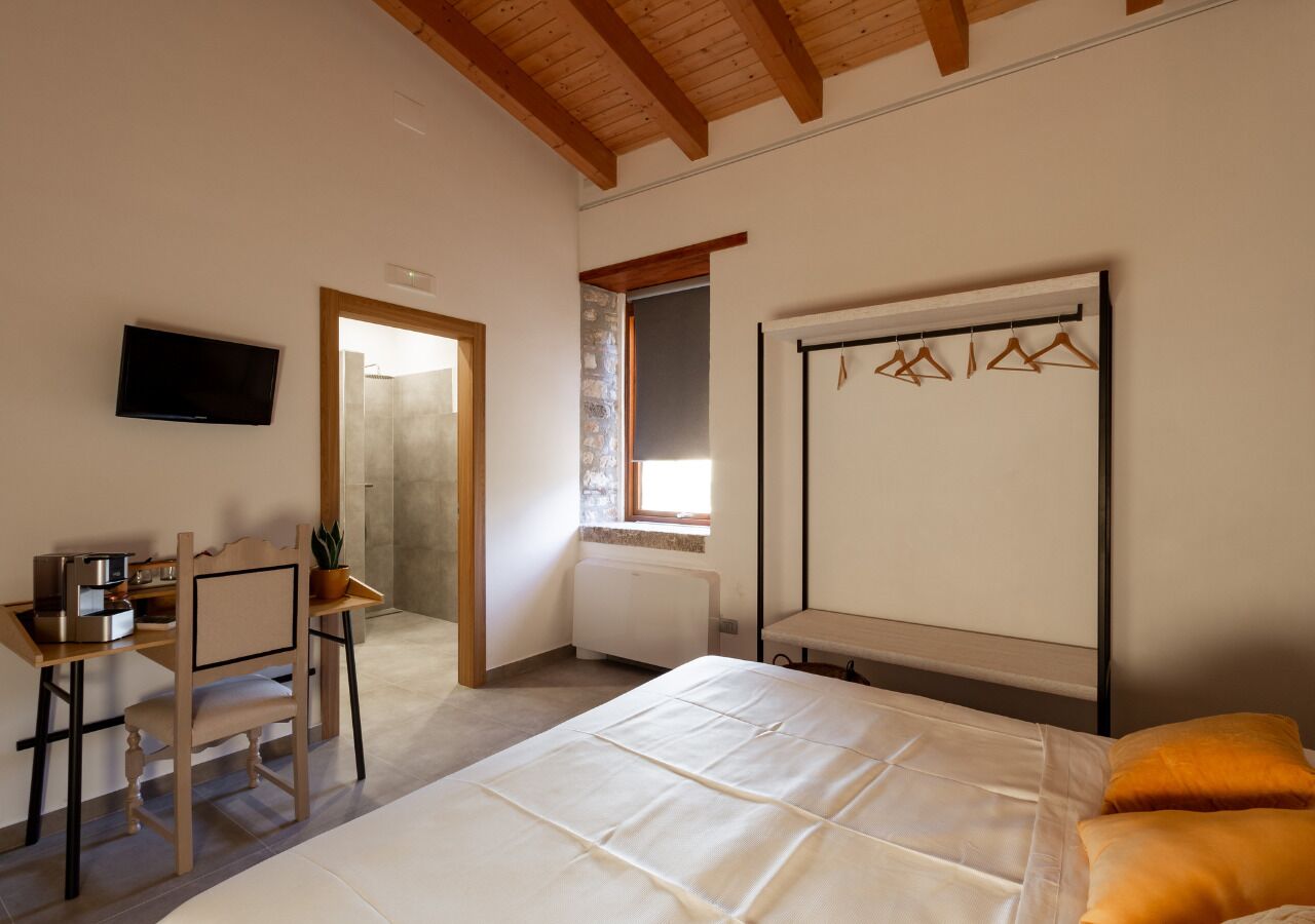 A bedroom with a bed, a desk with a chair, a television, and a window.