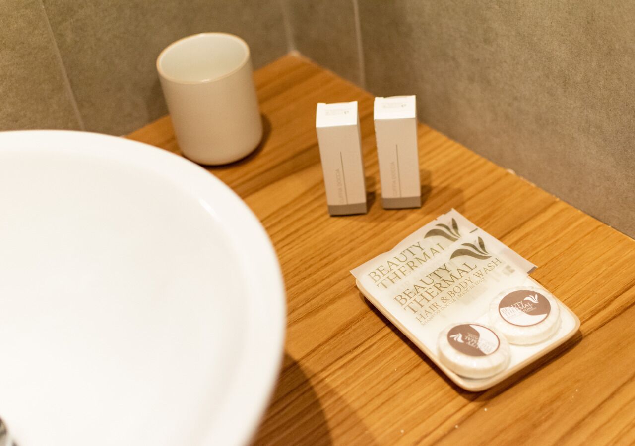 Un baño con un lavamanos blanco, una bandeja de madera y un paquete de crema de limpieza para cabello y cuerpo Beauty Thermal.
