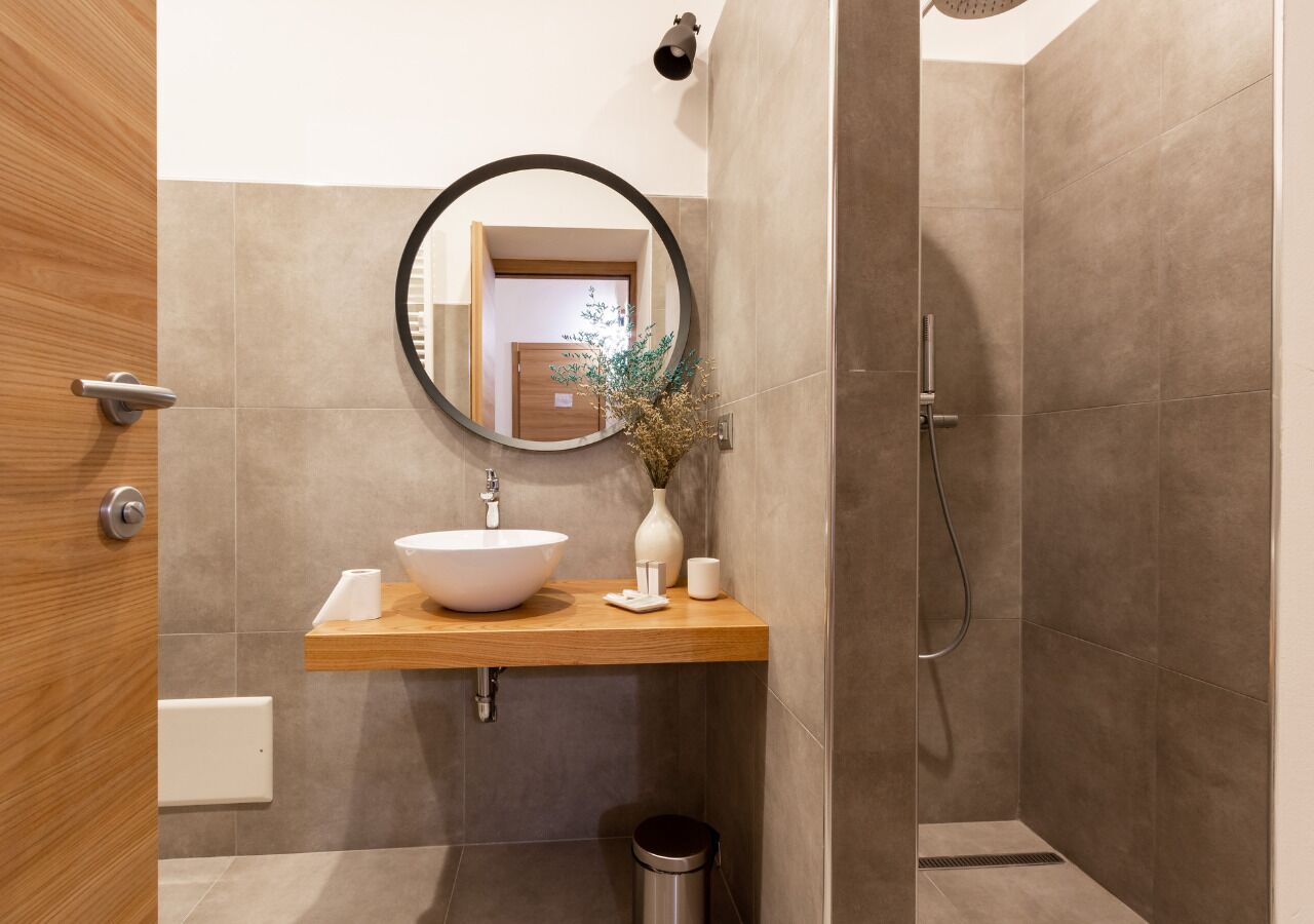 Un baño con tocador de madera, un espejo redondo, un lavabo blanco y una zona de ducha.