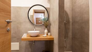 Un baño con tocador de madera, un espejo redondo, un lavabo blanco y una zona de ducha.