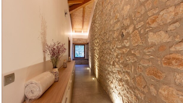 A hallway with a stone wall, wooden ceiling beams, and a view to a room with a window. - Tenuta San Martino (Nusco)