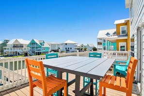 A wooden deck with a table and chairs, overlooking a row of colorful houses by the water. - Lagoon Front | Boat Launch, Pier and Beach Access | Pet Friendly (Gulf Shores)