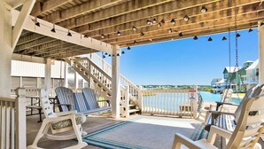 Um deck de madeira com cadeiras de balanço e vista para uma piscina e casas.