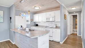 A kitchen with white cabinets, a granite countertop, a built-in oven, and a microwave. - Gulf Front | Pet Friendly | Fort Morgan Retreat (Gulf Shores)