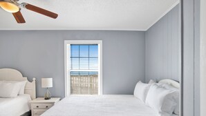 A bedroom with a bed, nightstand, lamp, window, and ceiling fan. - Gulf Front | Pet Friendly | Fort Morgan Retreat (Gulf Shores)