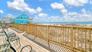 A wooden deck with chairs, a blue building, and a beach view. - Gulf Front | Pet Friendly | Fort Morgan Retreat (Gulf Shores)