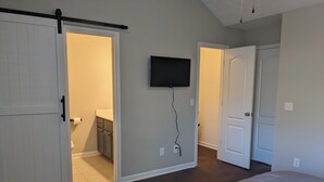 Un dormitorio con una cama grande, un armario de puertas correderas, un televisor montado en la pared y un baño visible a través de la puerta.