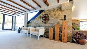 Ein geräumiges Zimmer mit Steinwand, Holzbalkendecke, einem weißen Sofa und einer großen Vase mit Blumen.