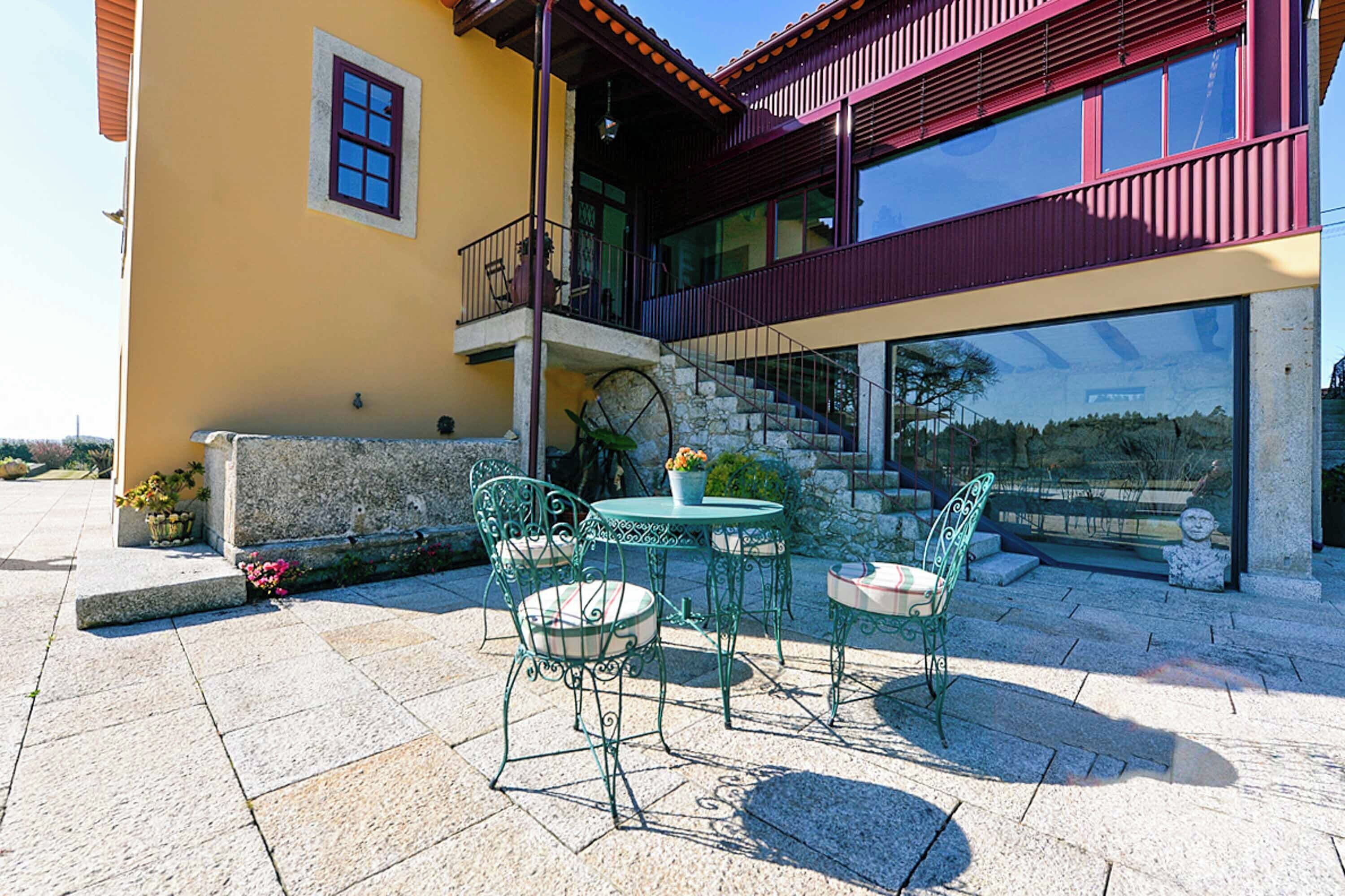 An outdoor patio with a table and chairs, a small garden area, and a building with a balcony.