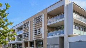 Un immeuble résidentiel à plusieurs étages, doté de balcons, d’un garage et surplombant un ciel dégagé.