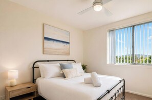 A bedroom with a bed, a nightstand, a ceiling fan, a window with a view, and a painting on the wall. - Caves Beach Retreat - close to beach and shops (Caves Beach)