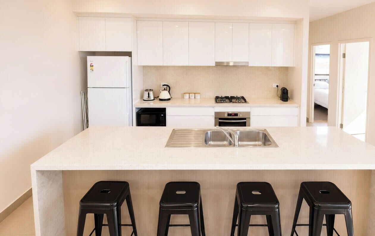A modern kitchen with white cabinets, a central island with bar stools, a built-in oven, and a stainless steel sink.