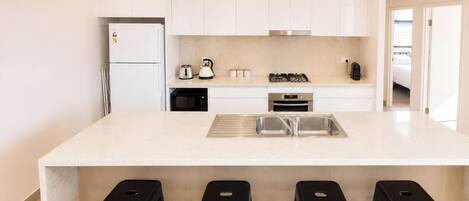 A modern kitchen with white cabinets, a central island with bar stools, a built-in oven, and a stainless steel sink.