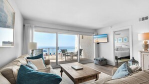 A spacious living room with a large sofa, a coffee table, and a balcony with a view of the beach. - Beautiful, Fully Renovated condo at Beach House (Miramar Beach)
