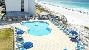 A pool area with lounge chairs and umbrellas, a beach in the background, and a tall building nearby. - Beautiful, Fully Renovated condo at Beach House (Miramar Beach)