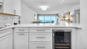 A modern kitchen with white cabinetry, a built-in oven, and a large window offering a view of the sea. - Beautiful, Fully Renovated condo at Beach House (Miramar Beach)