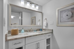 A bathroom with a marble countertop, a large mirror, a towel ring, and a framed artwork on the wall.
