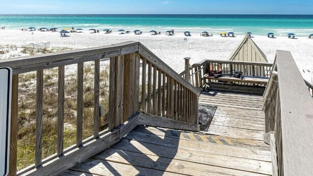A wooden deck leading to a beach with umbrellas and beach chairs. - Beautiful, Fully Renovated condo at Beach House (Miramar Beach)