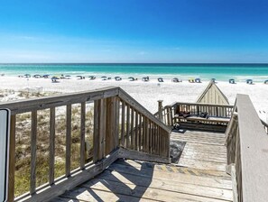 A wooden deck leading to a beach with umbrellas and beach chairs.