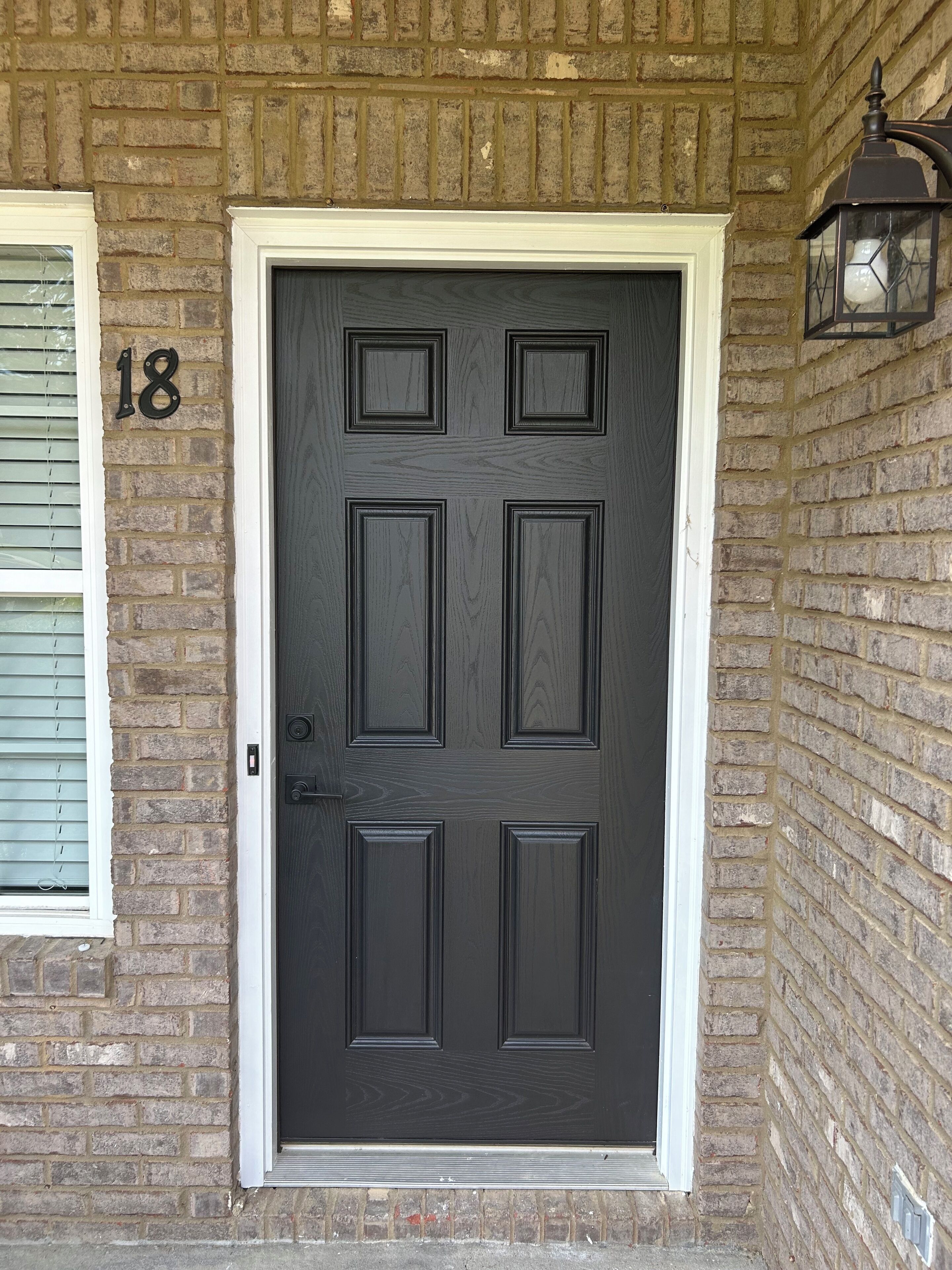A dark wooden door with a white frame, set in a brick wall.