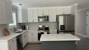 Cozinha moderna com armários brancos, eletrodomésticos de aço inoxidável e bancada de mármore.