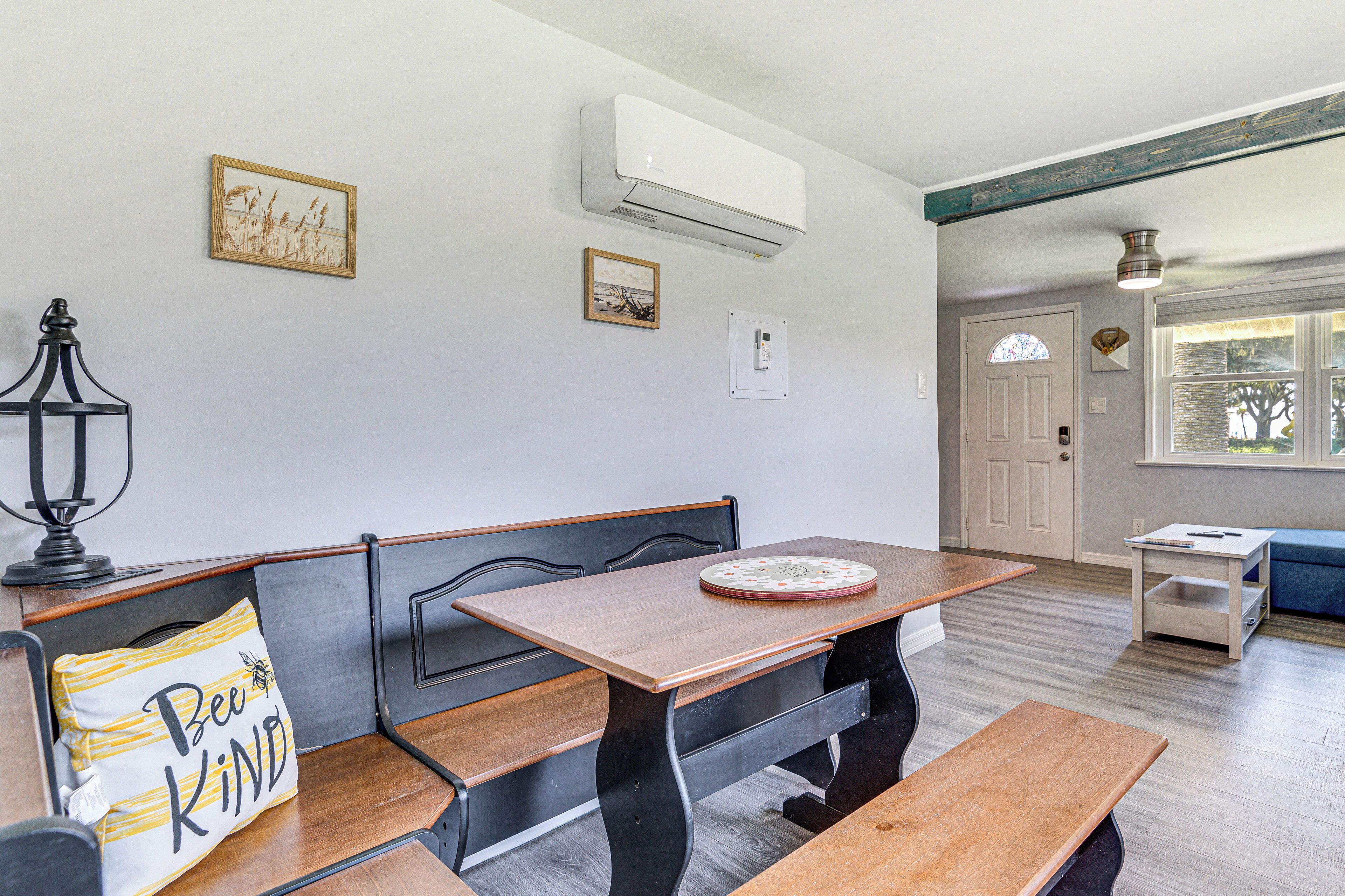 A dining area with a wooden table and benches, an air conditioning unit above, and framed pictures on the wall.