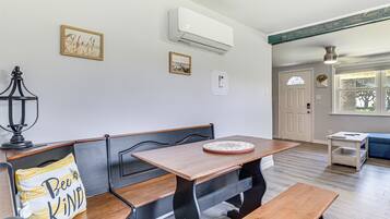 A dining area with a wooden table and benches, an air conditioning unit above, and framed pictures on the wall.